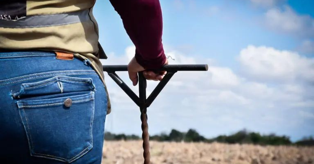 Persona usando un taladro de tierra en un campo durante un operativo de búsqueda de desaparecidos.
