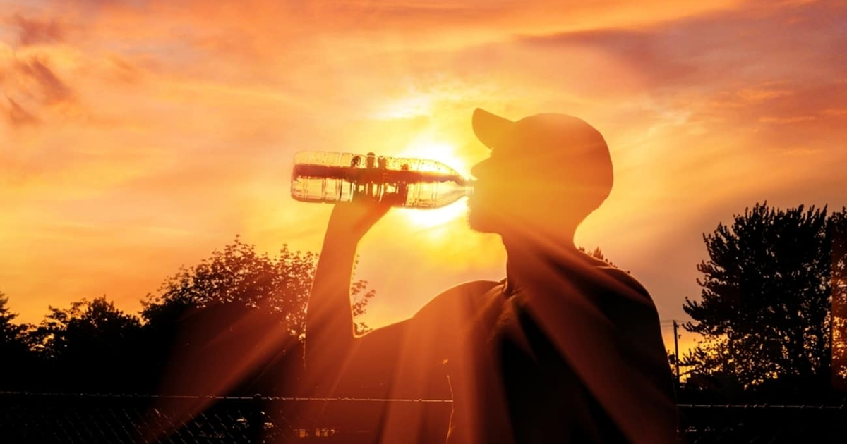 Persona bebiendo agua al atardecer, simbolizando hidratación durante olas de calor en Sinaloa.