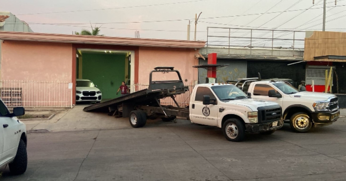 Escena urbana en Culiacán con casa rosa, automóvil blanco y grúa en operativo de cateo.