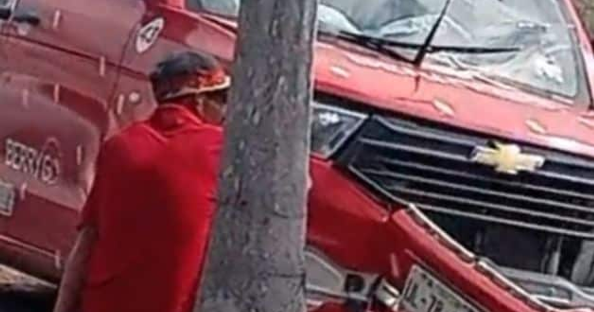 Persona vestida de rojo junto a un árbol con un vehículo Chevrolet rojo dañado al fondo, tras accidente en Marina Mazatlán.