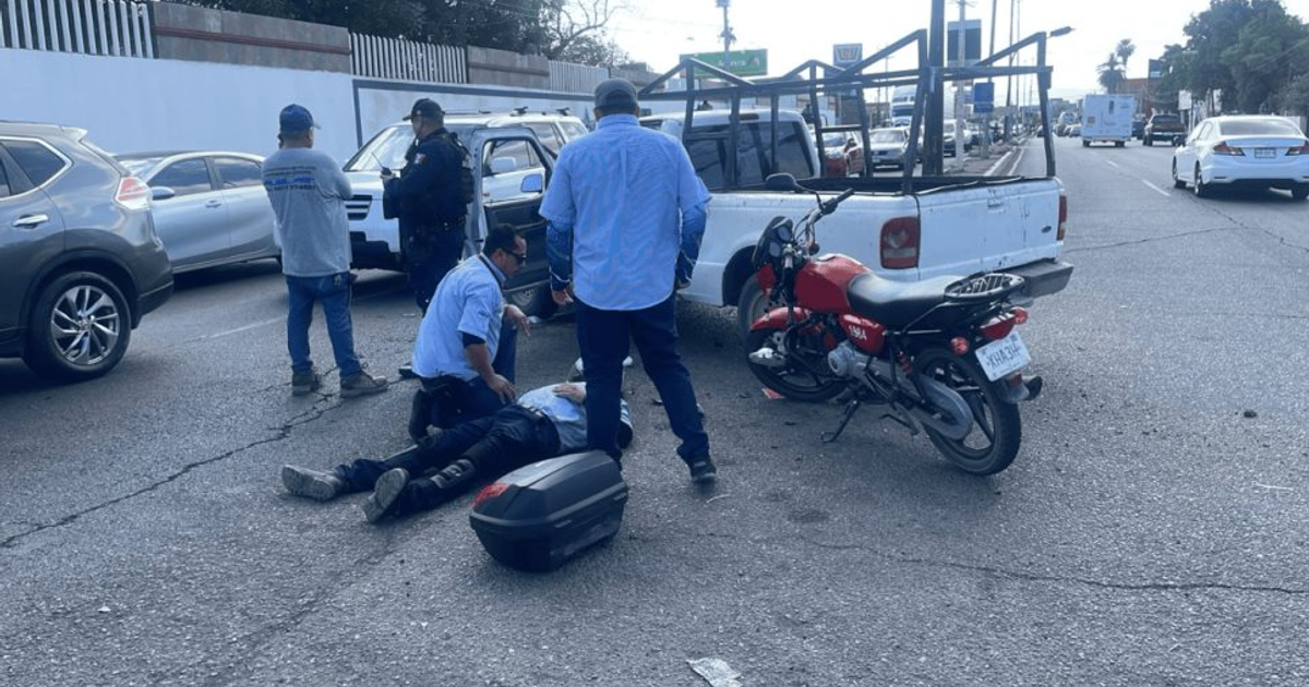Escena de accidente de tráfico en calzada Aeropuerto con camioneta blanca y motocicleta roja involucradas, personas asistiendo al herido y presencia policial.