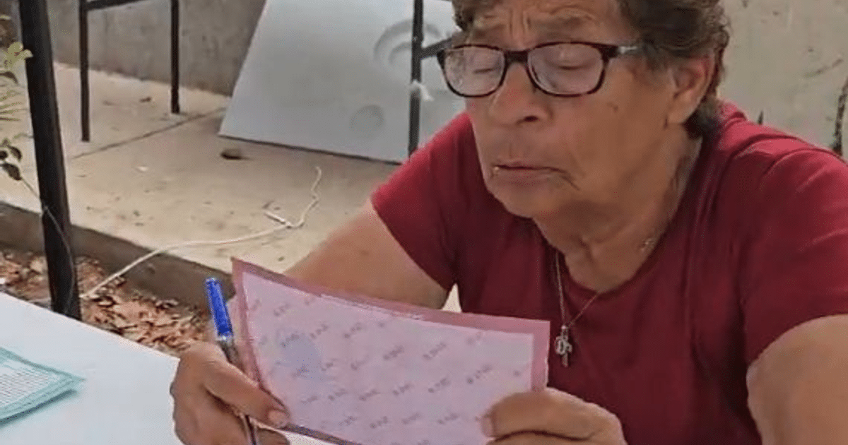 Mujer mayor con gafas sosteniendo un papel rosado en un entorno urbano, simbolizando los desafíos electorales.