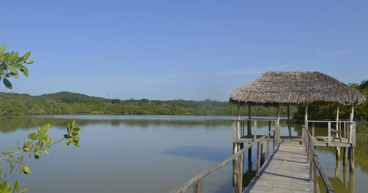 Muelle de madera en el Estero del Yugo con colinas verdes y refugio de palma
