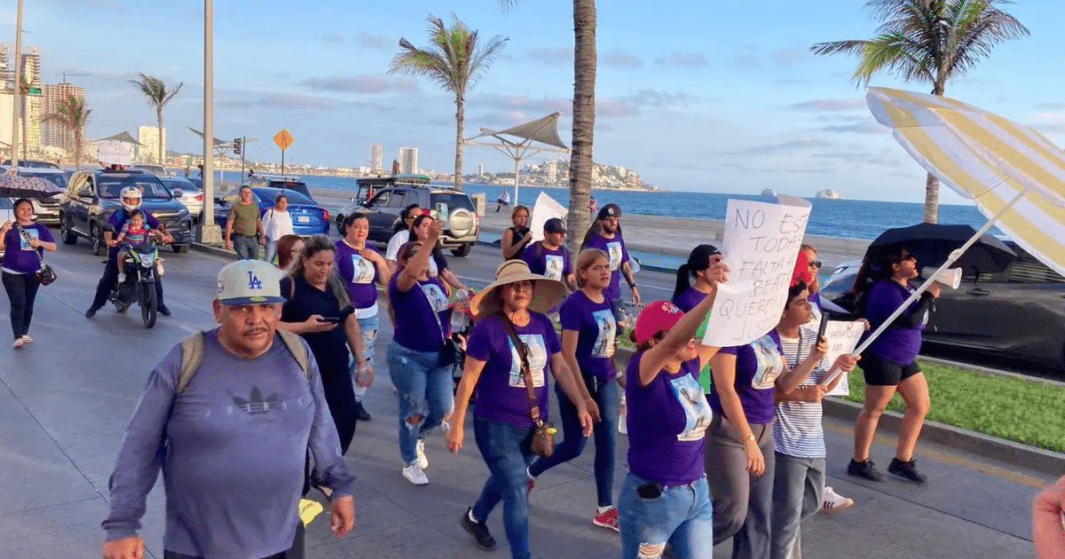 Mujeres marchando en Mazatlán por justicia para Ana Beatriz, con camisetas moradas y carteles, en un entorno costero.