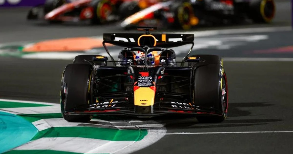 Coche de Fórmula 1 en circuito urbano nocturno con otros vehículos al fondo