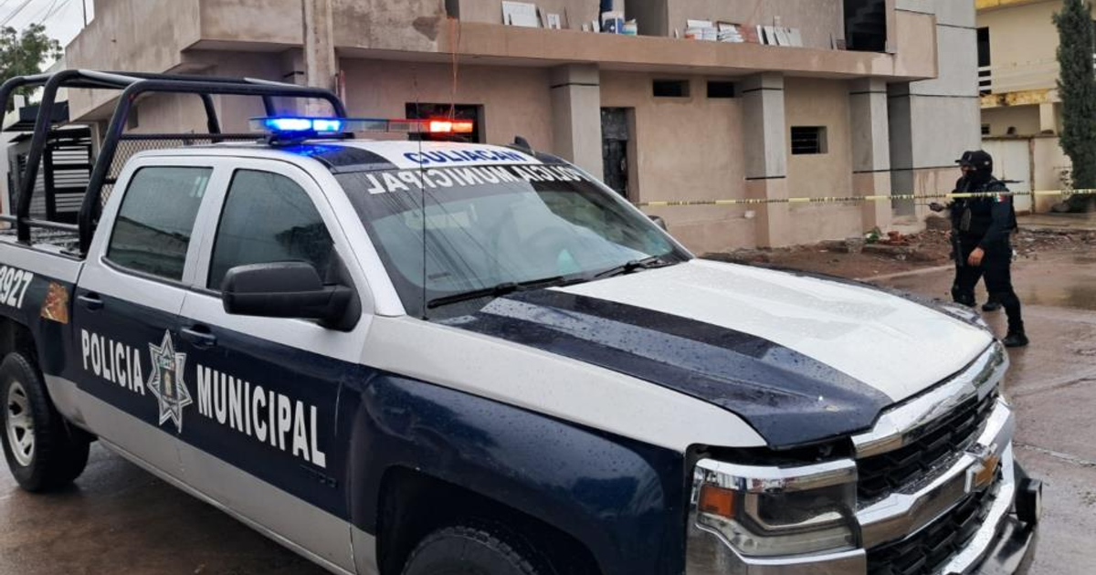 Camioneta de policía con luces activadas en escena de crimen en Culiacán, con oficial y cinta de seguridad amarilla bajo lluvia.