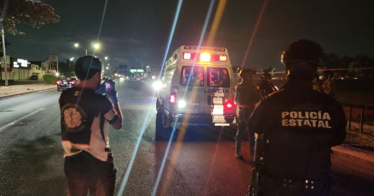 Ambulancia con luces encendidas en escena nocturna de emergencia en Culiacán, con presencia de policías y civiles.