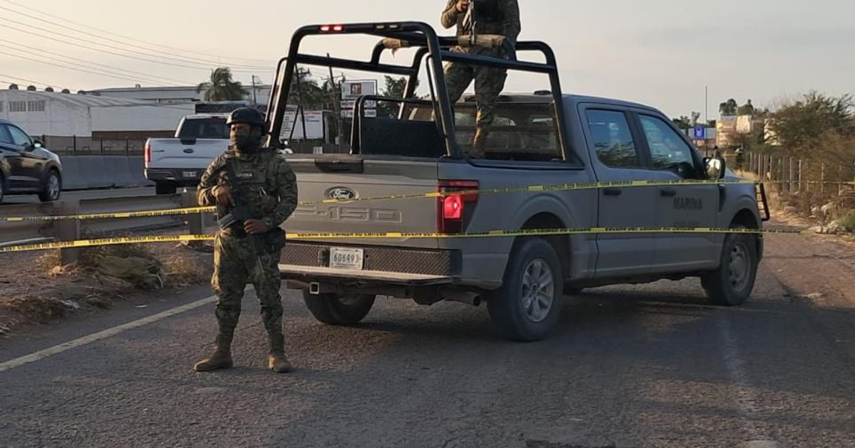Operativo de seguridad en carretera con militar armado junto a vehículo pickup, cinta amarilla delimita la escena.