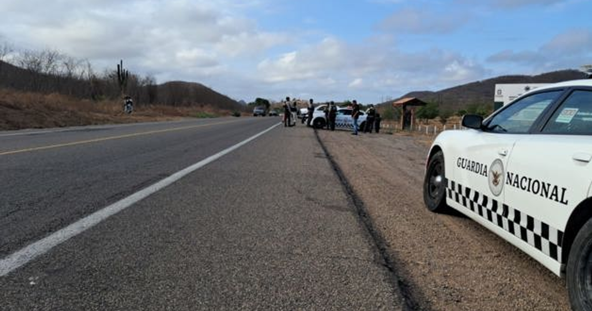 Carretera desierta con vehículo policial y personas reunidas en un entorno rural nublado.