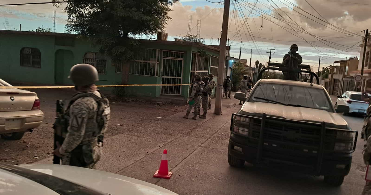 Grupo armado en operativo de seguridad en Sinaloa, con vehículos y cinta amarilla en escena urbana.