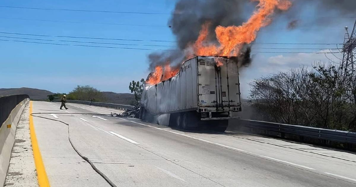 Camión en llamas en carretera con humo denso y persona cercana