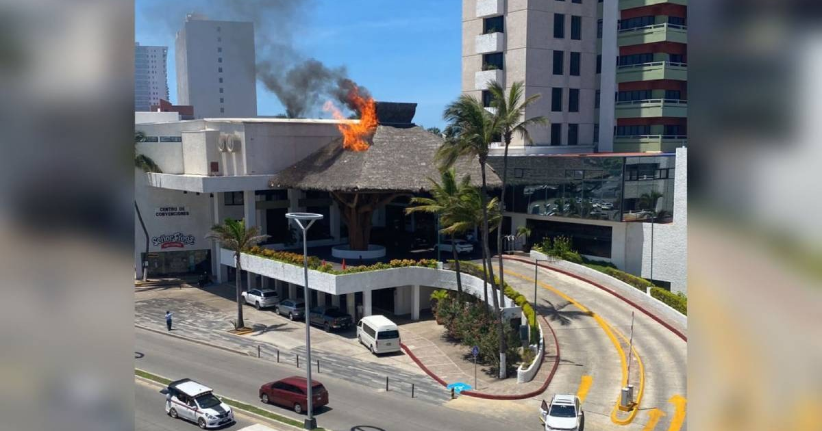 Techo de palma en llamas en el hotel El Cid, Mazatlán, con humo y edificios circundantes.