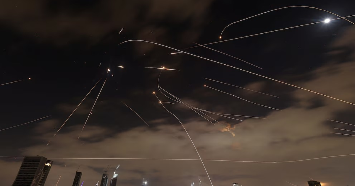 Cielo nocturno con trazos de luz de misiles sobre edificios, reflejando la ofensiva iraní contra Israel.