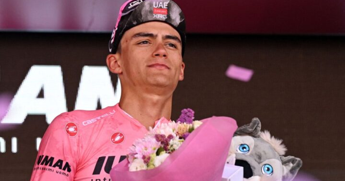 Persona con camiseta rosa y gorra de ciclismo sosteniendo flores y peluche en celebración.