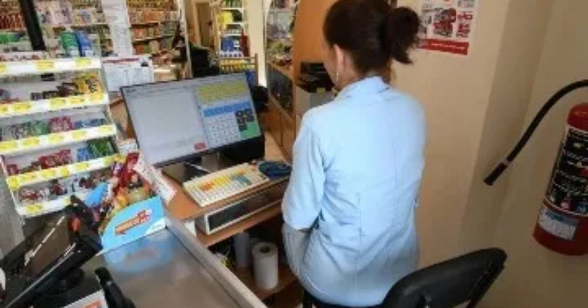 Cajera sentada en área de caja de tienda con computadora y estantes de productos, destacando la Ley Silla.
