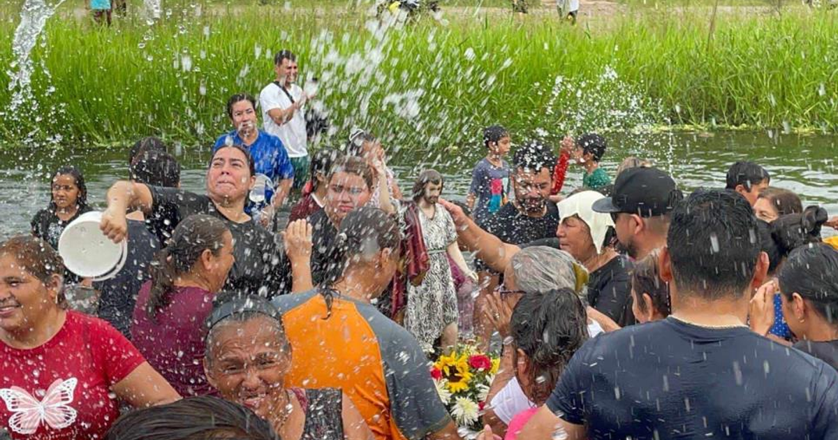 Grupo de personas celebrando en un río bajo la lluvia, con una estatua religiosa visible.