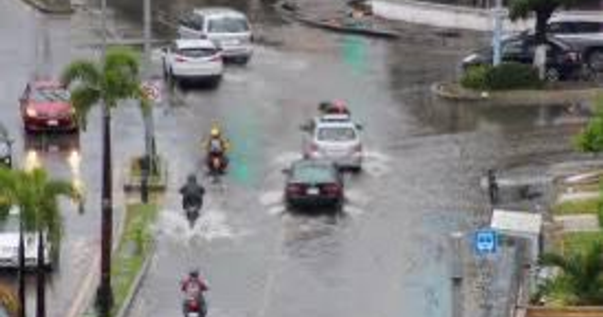 Calle inundada en Sinaloa con vehículos circulando bajo la lluvia