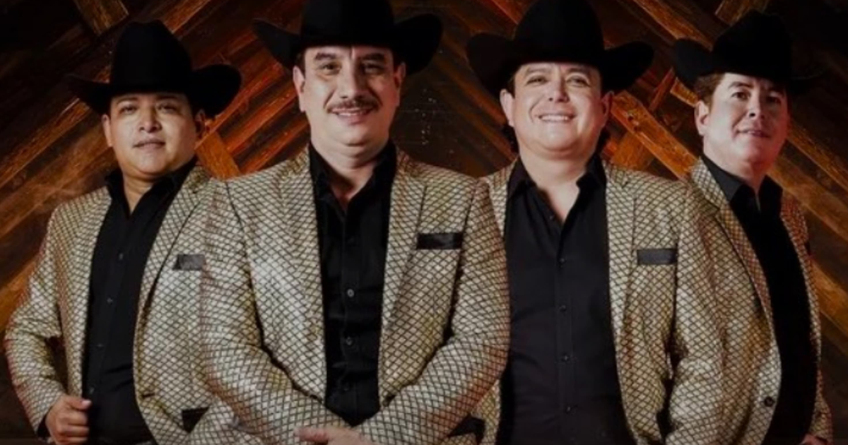 Los Alegres del Barranco posando con trajes brillantes y sombreros, fondo de madera.