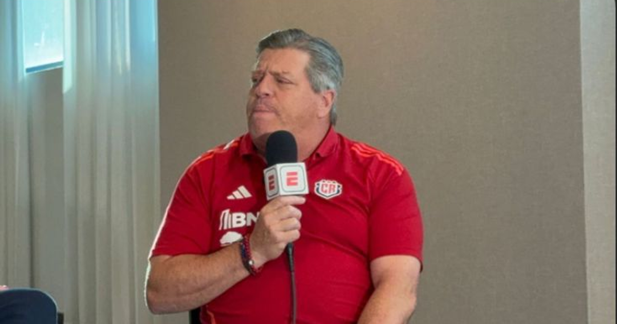 Miguel Herrera en conferencia de prensa con camisa roja y micrófono en mano.