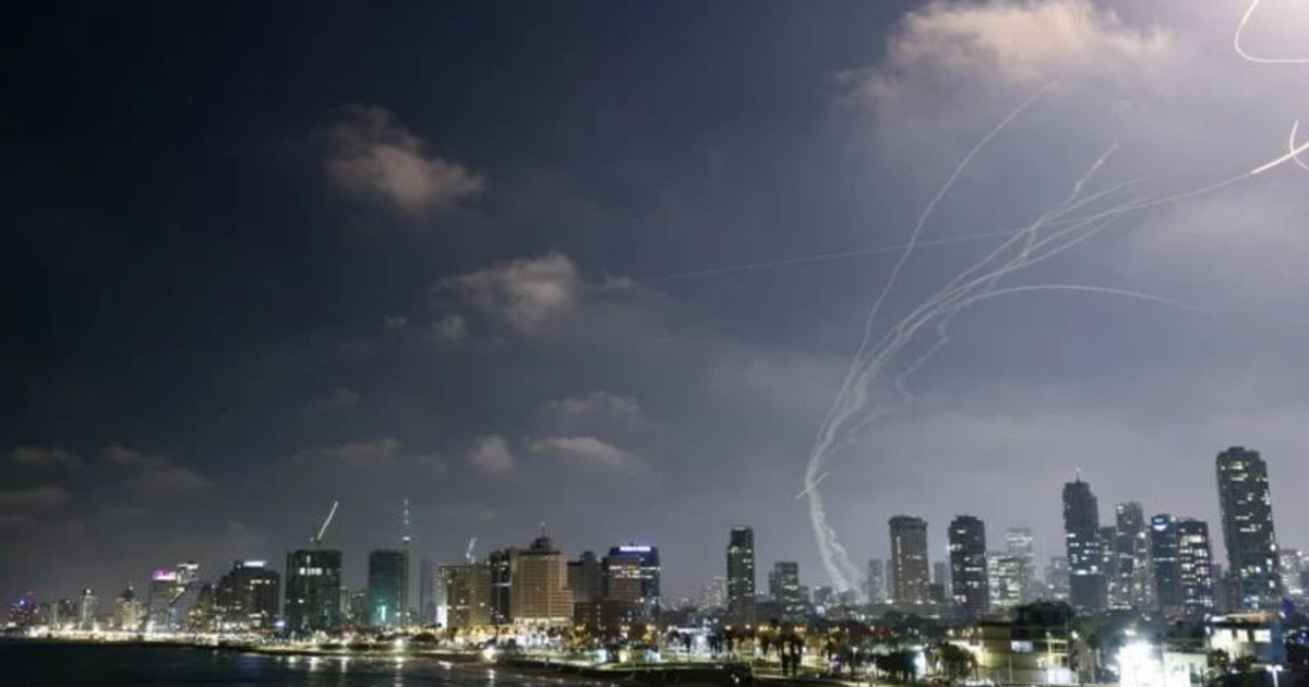 Paisaje urbano nocturno con rastros de misiles en el cielo, reflejando un conflicto militar en Medio Oriente.