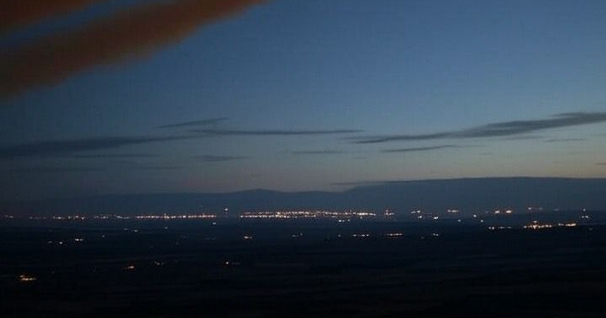 Paisaje al anochecer con luces urbanas y montañas en el horizonte.