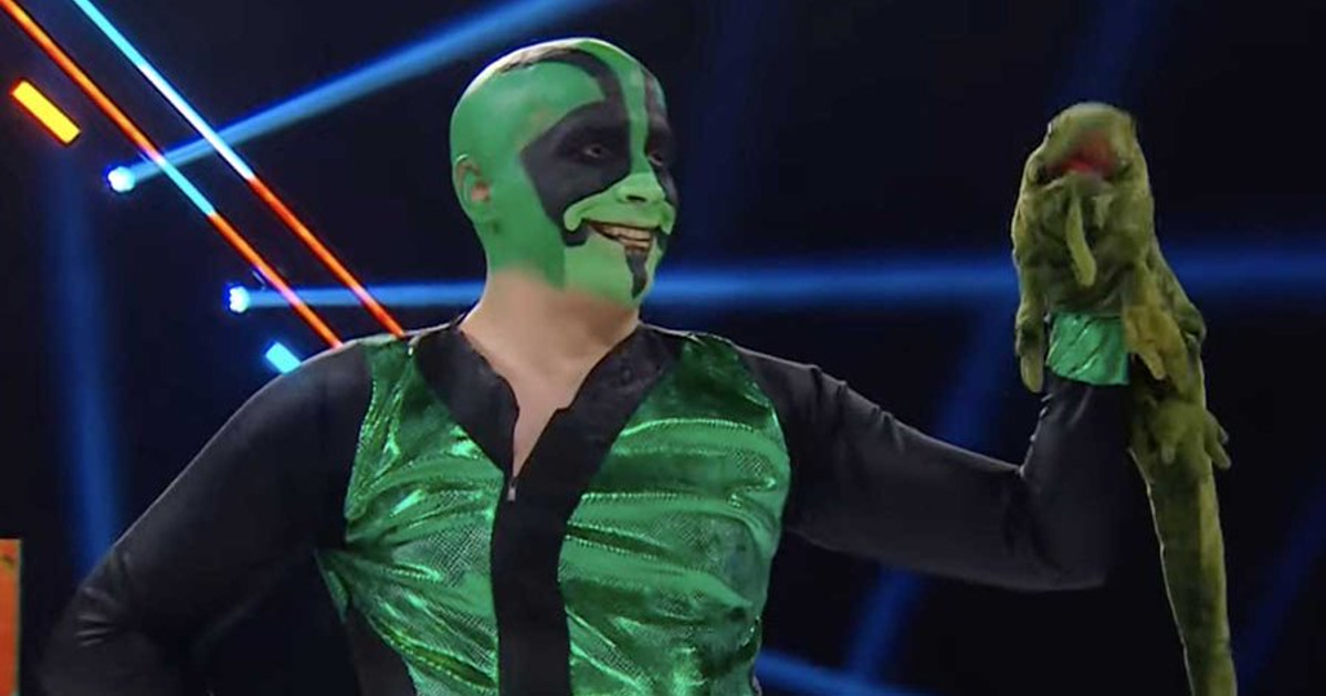 Mr. Iguana en el evento Worlds Collide, vestido de verde y negro, sosteniendo su marioneta 'Yesca'.