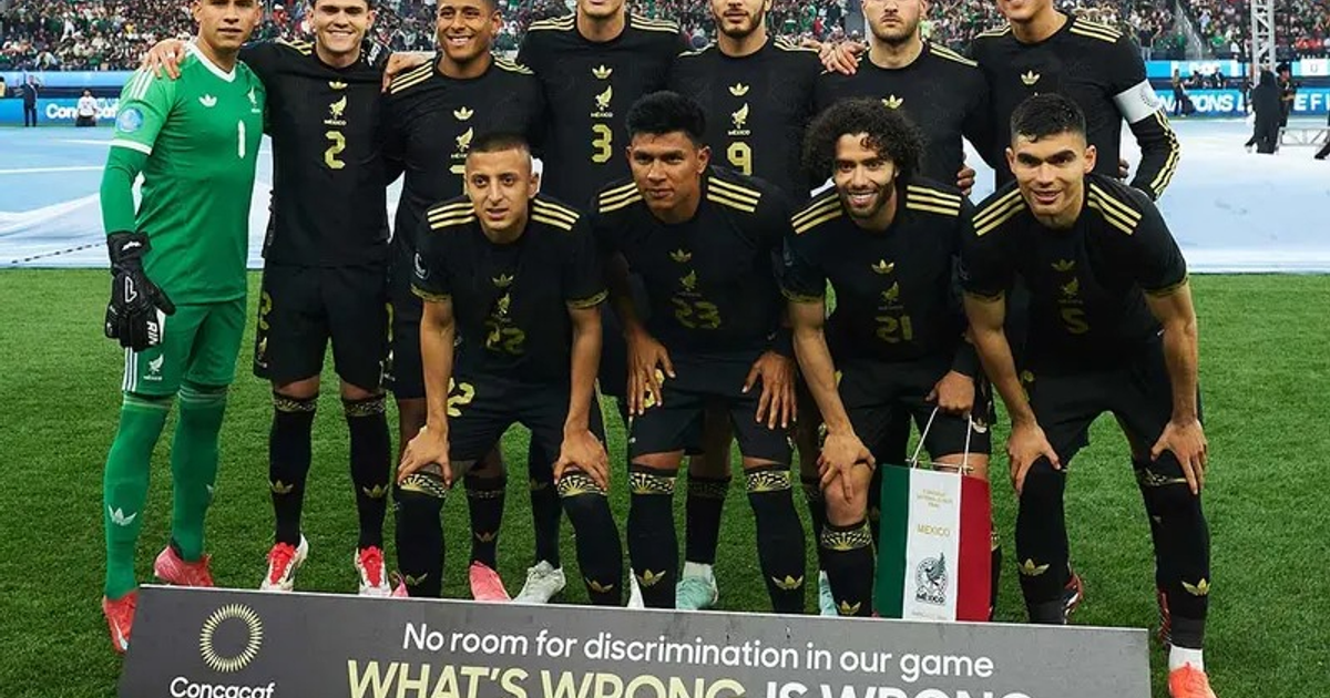Equipo de fútbol con uniformes negros y dorados posando en el campo, portero en verde, cartel contra la discriminación y bandera mexicana en la Copa Oro 2025.