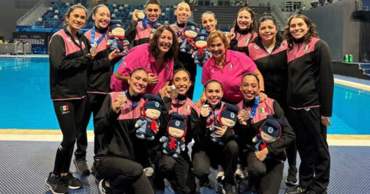 Equipo mexicano de nado artístico celebra medalla de bronce en la Copa del Mundo en Xi’an, China, posando con medallas y muñecos frente a una piscina.
