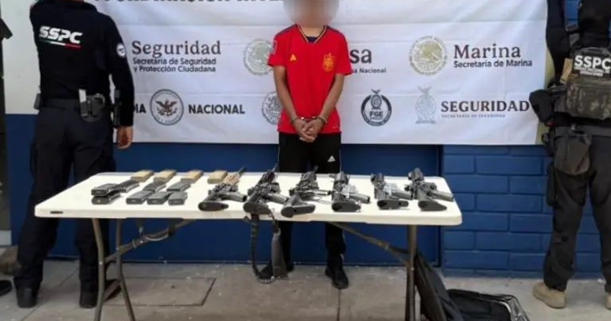 Persona esposada frente a mesa con armas incautadas durante intervención policial en Campo Romero.
