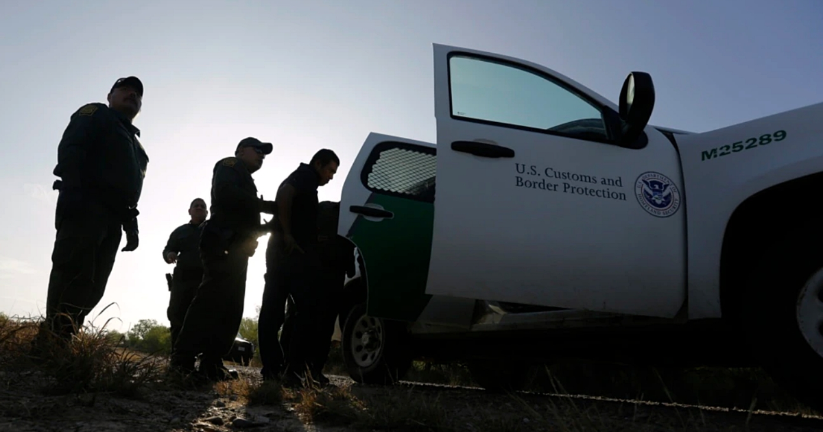 Agentes de la Patrulla Fronteriza de EE.UU. junto a un vehículo de la CBP interactuando con una persona al aire libre.