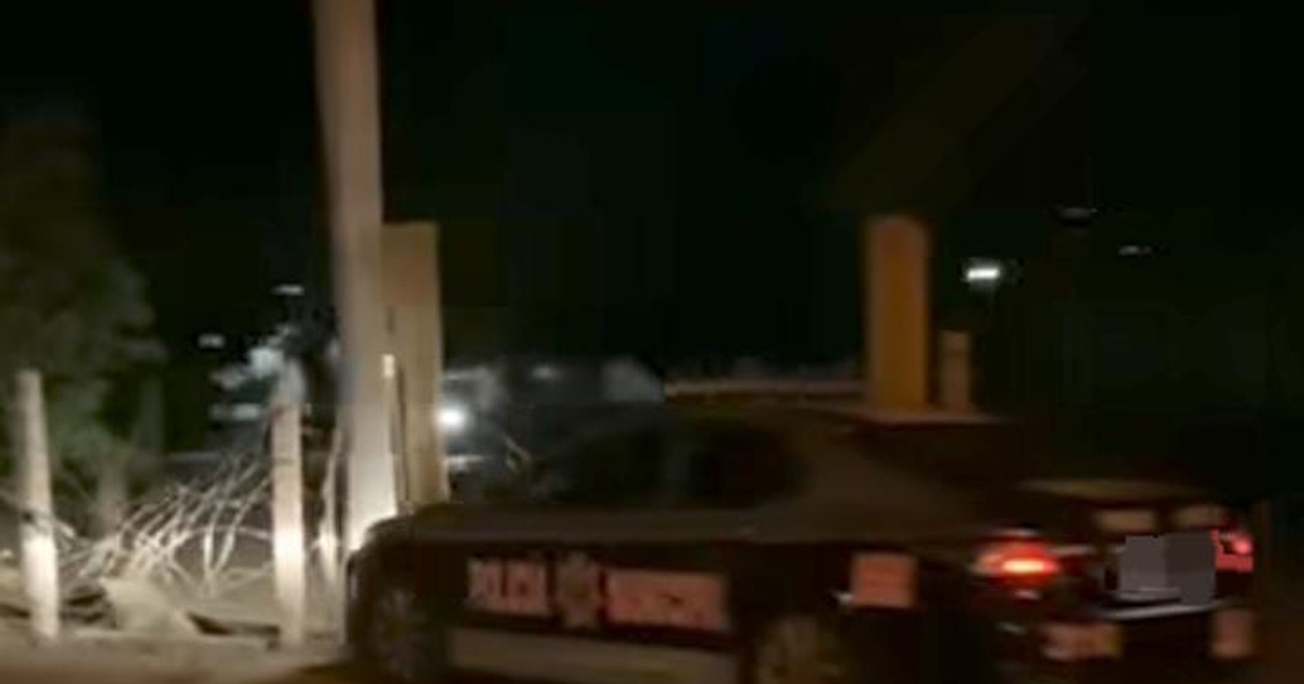 Automóvil de policía estacionado de noche en Navolato, cerca de una entrada con postes y cercas.