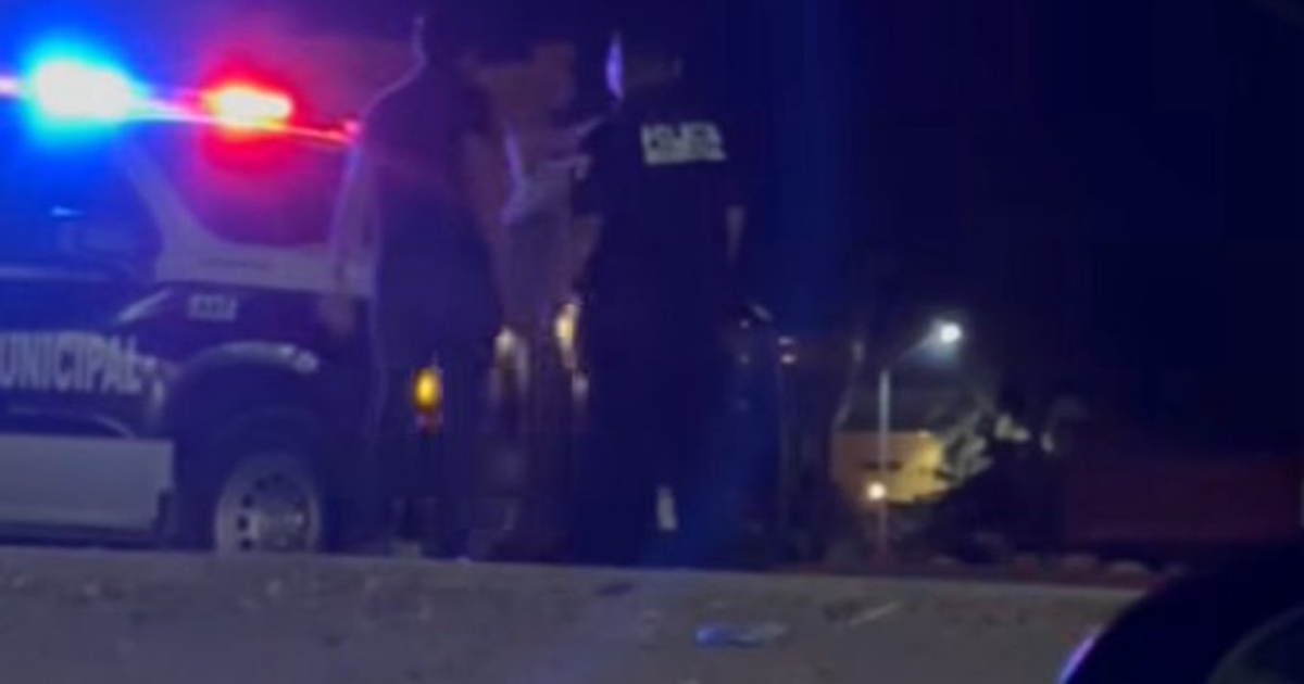 Vehículo policial con luces parpadeantes en una escena nocturna de Los Mochis, con dos personas cerca del automóvil.