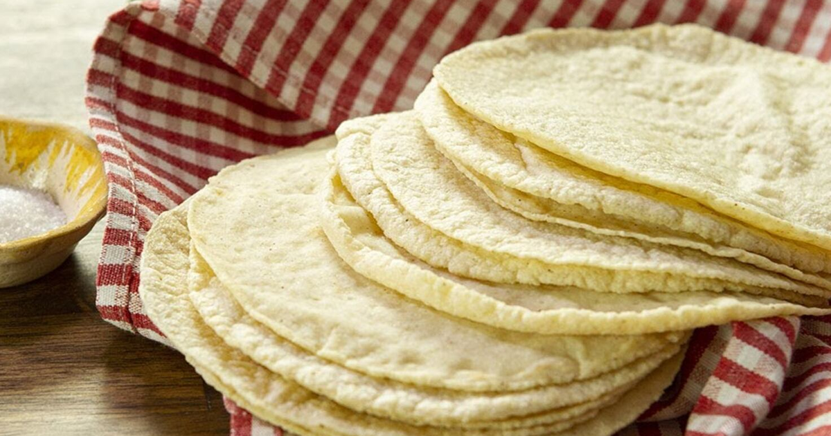 Tortillas apiladas sobre un paño de cocina a rayas con un plato de sal al lado.