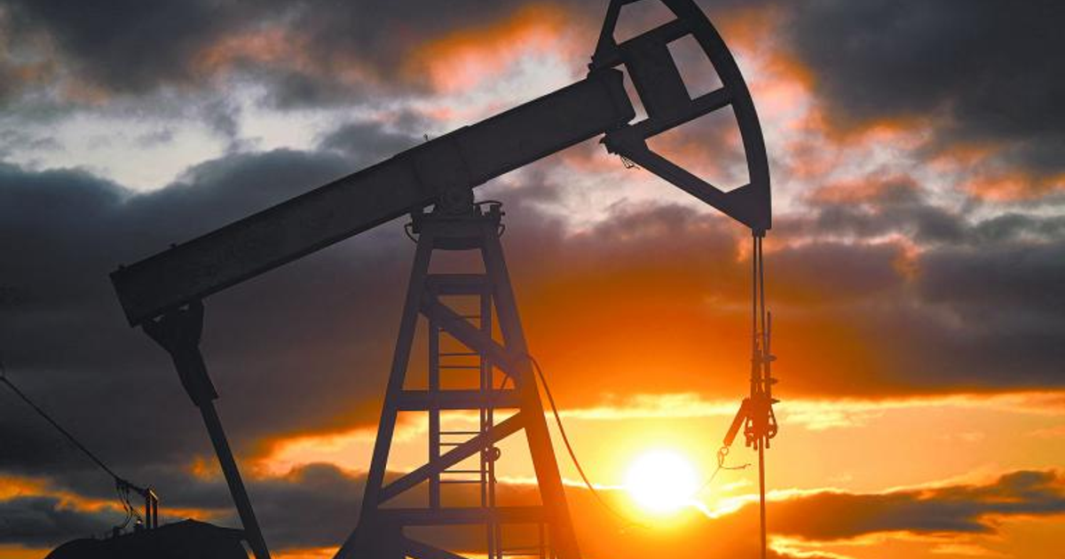 Silueta de bomba de extracción de petróleo al atardecer con cielo anaranjado y nubes.