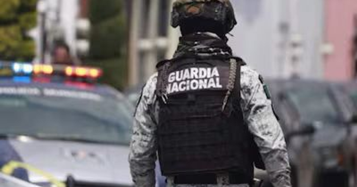 Miembro de la Guardia Nacional con chaleco en entorno urbano, patrullas con luces encendidas, relacionado con reforma legislativa.