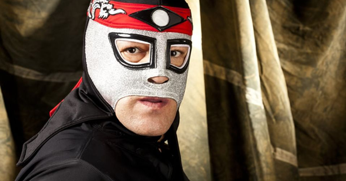 Luchador enmascarado con máscara plateada y traje negro en pose seria