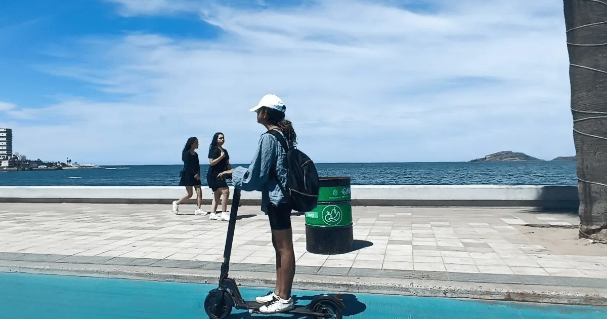 Persona en patinete eléctrico cerca de la costa con mar y cielo despejado de fondo