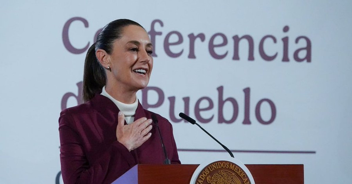 Mujer en podio hablando en la Conferencia de Pueblo, con chaqueta púrpura y fondo de evento.