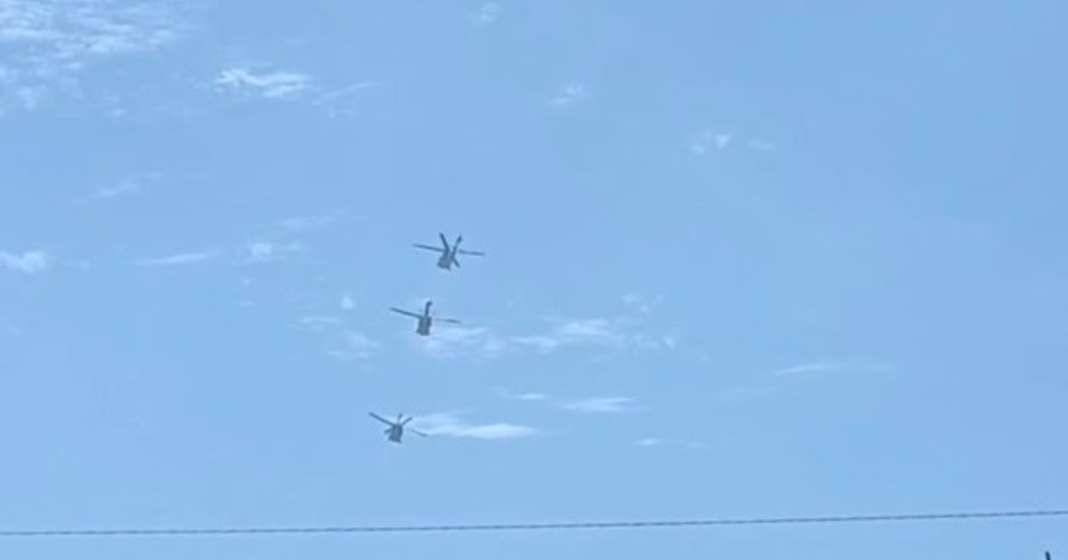 Tres helicópteros Black Hawk en formación sobre un cielo azul con nubes.