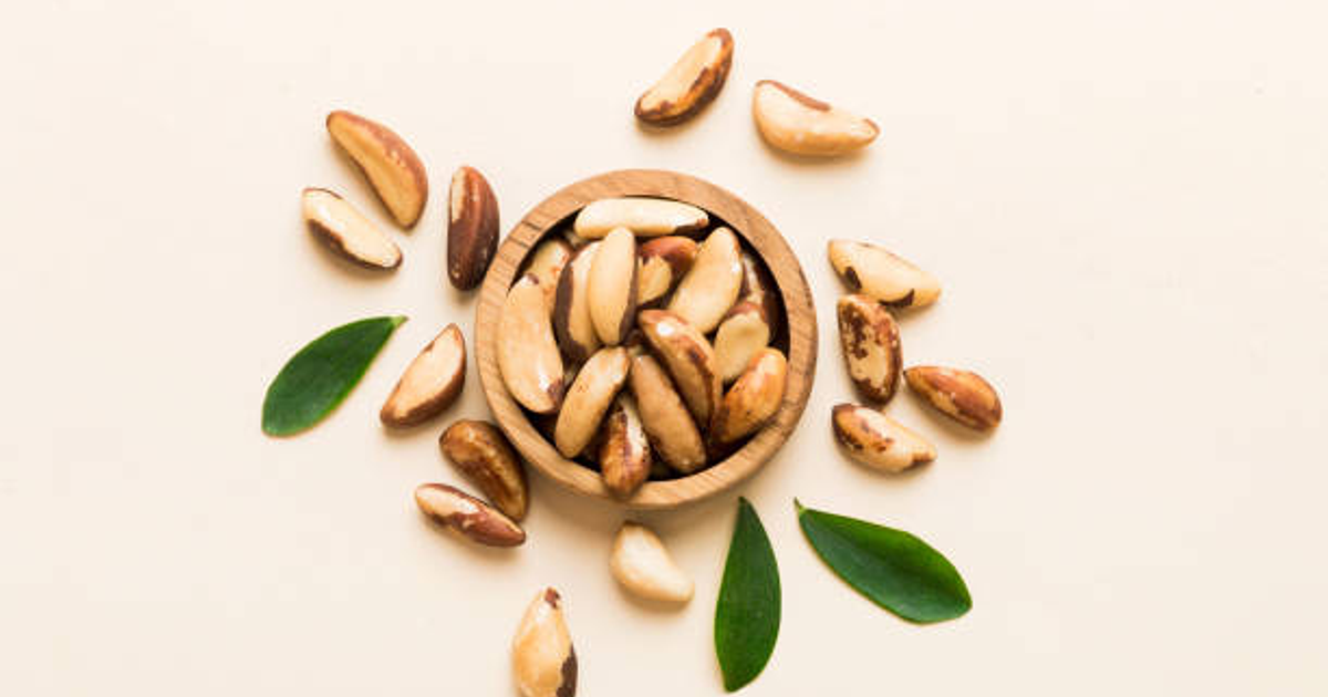 Nueces de Brasil en un tazón de madera rodeado de hojas verdes sobre fondo claro.