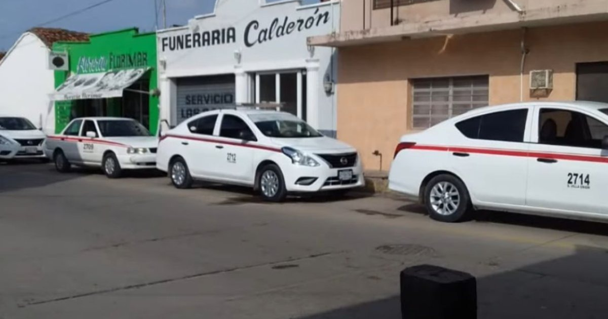 Taxis blancos con franjas rojas estacionados frente a Funeraria Calderón en Villa Unión