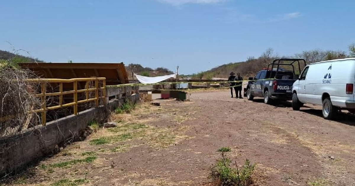 Área rural con camino de tierra, estructura en desuso, valla amarilla y vehículos policiales en Sinaloa.