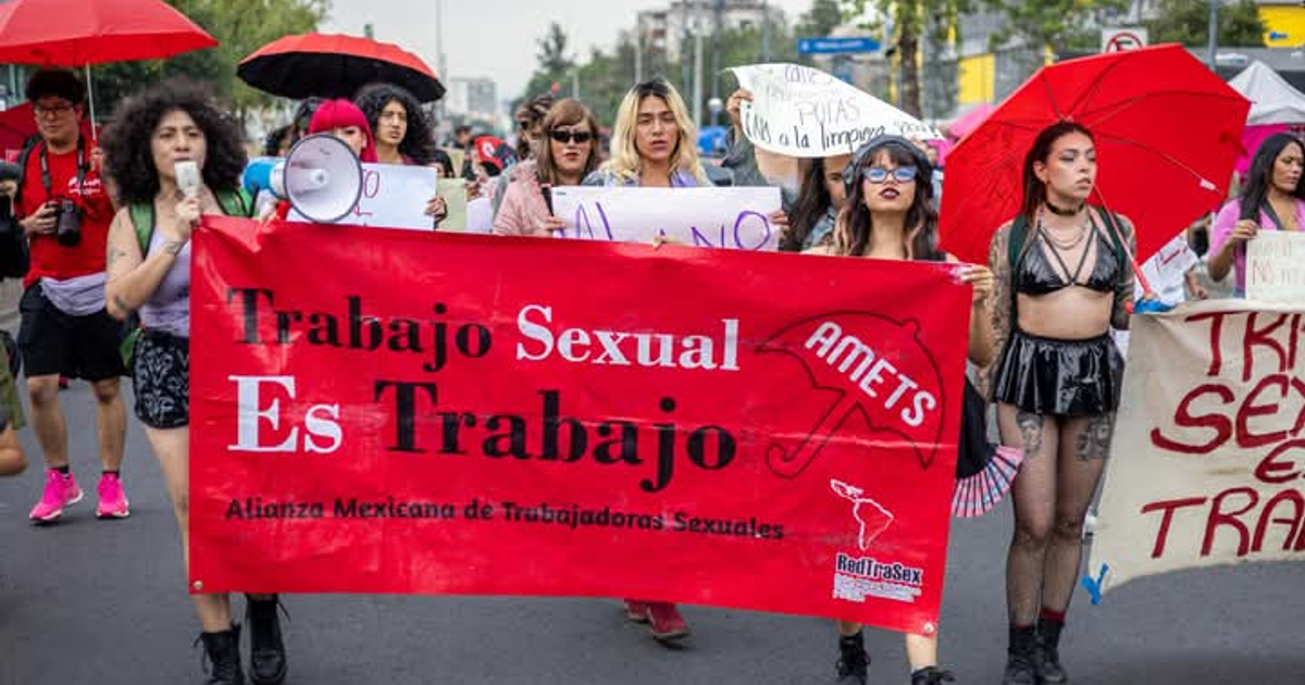 Manifestación en CDMX por derechos de trabajadoras sexuales con pancarta roja y paraguas.