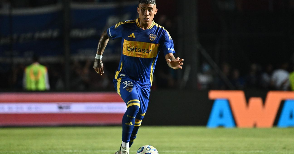 Jugador de Boca Juniors corriendo hacia el balón en un campo de juego, con camiseta azul y detalles amarillos.
