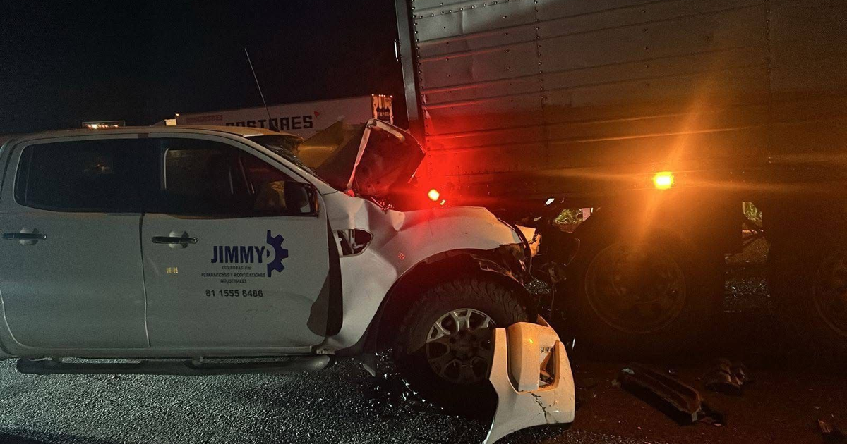 Accidente de tránsito nocturno en carretera con camioneta blanca dañada tras colisión con tráiler.