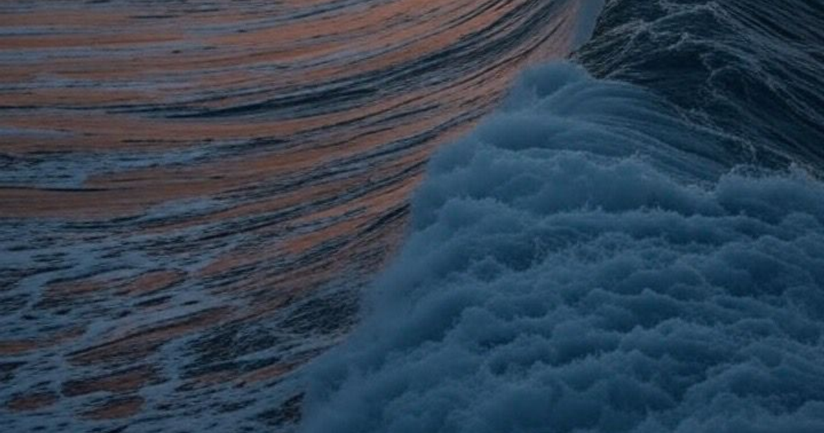 Olas del mar con espuma y reflejos de atardecer, simbolizando tranquilidad tras alerta de tsunami cancelada.