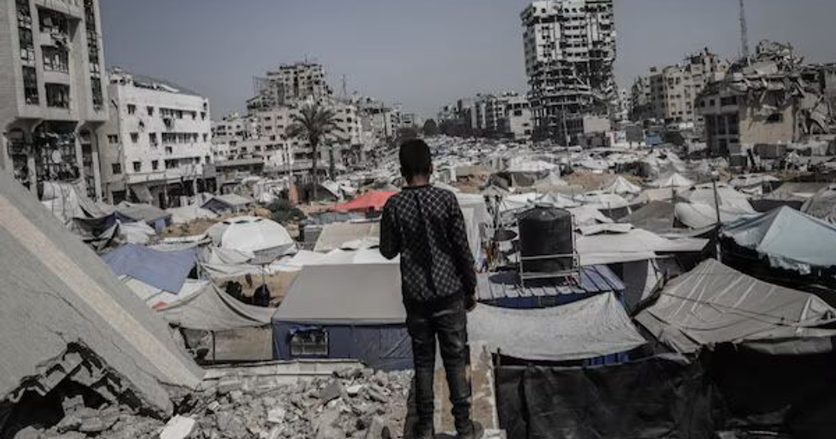 Vista aérea de un campamento en Gaza con edificios en ruinas al fondo, reflejando un contexto de crisis.