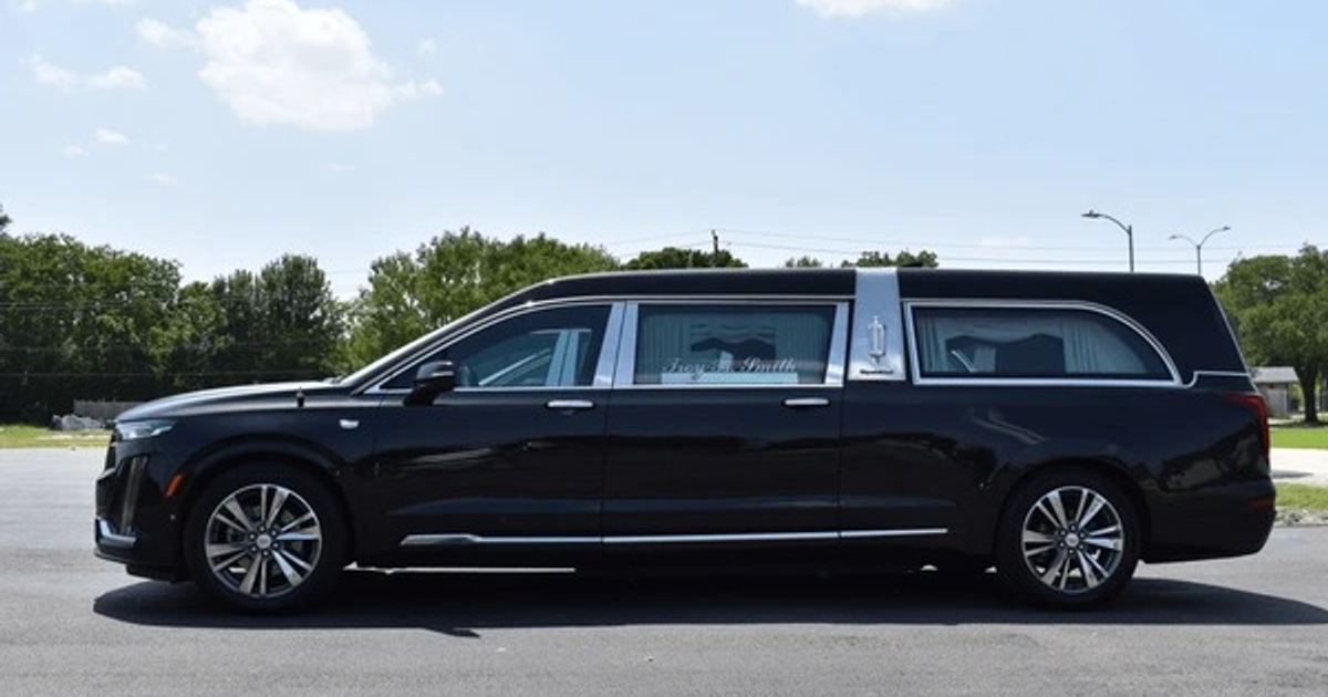 Limusina negra estacionada en área pavimentada con árboles y cielo despejado