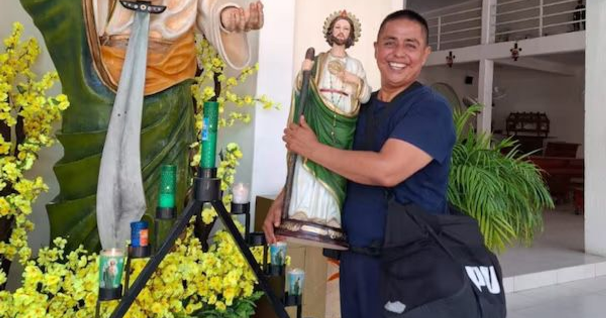 Hombre sosteniendo estatua religiosa con decoraciones florales y velas