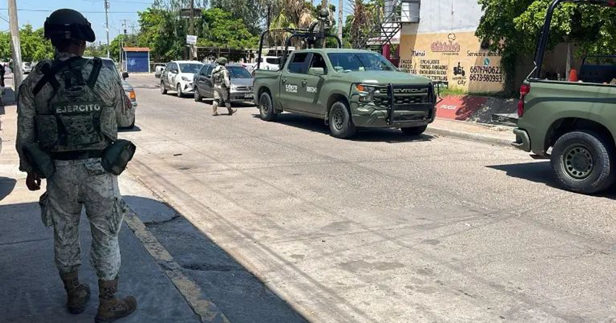 Soldado en uniforme militar patrullando una calle de Culiacán con vehículos y edificios de fondo.